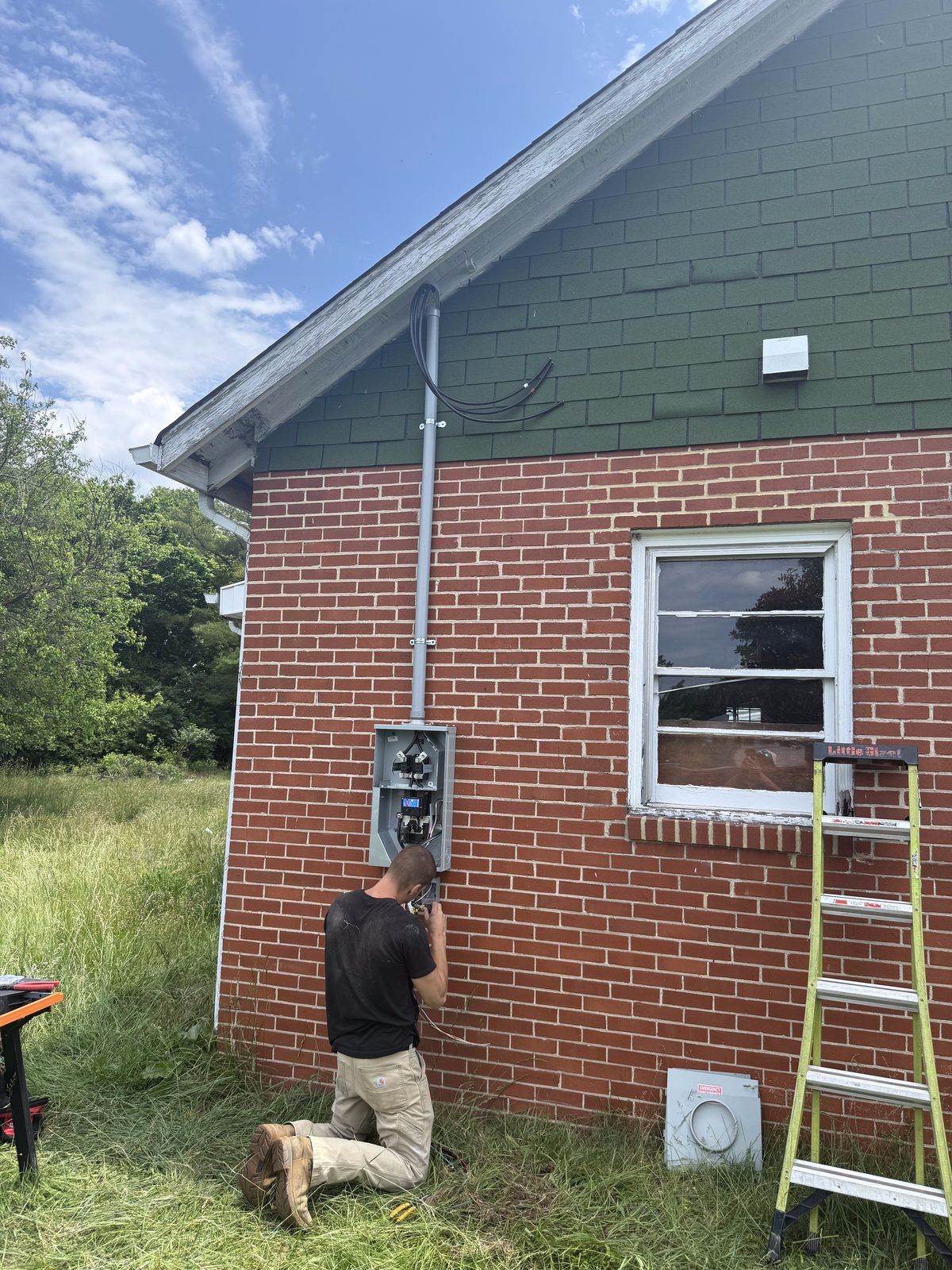 Electrician wiring a new meter base and service mast on a brick home